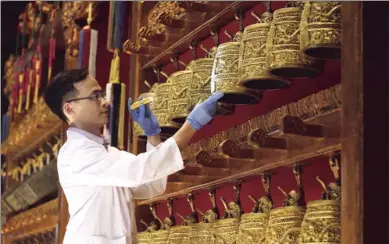  ?? ROY LIU / CHINA DAILY ?? A curator checks bronze bells with double-dragon handles and dragon and cloud design on the bodies — made in the 52nd year of the Kangxi’s reign (1713) in the Qing Dynasty (1644-1911) — from the Palace Museum collection on Tuesday. The exhibit is part...