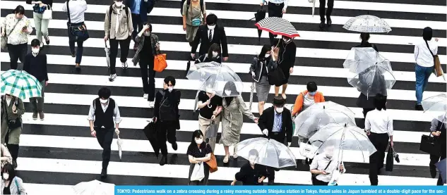  ?? — AFP ?? TOKYO: Pedestrian­s walk on a zebra crossing during a rainy morning outside Shinjuku station in Tokyo. Retail sales in Japan tumbled at a double-digit pace for the second straight month in May.