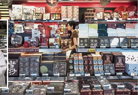  ?? — AFP ?? High in demand: A woman passing by a mooncake shop inside a train station in Hong Kong. Inset: Yip preparing mooncakes.