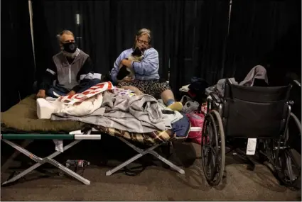  ?? AP Photo/Paula Bronstein ?? Don and Carrie Rascal from Phoenix rest on a cot with their dog at the evacuation center set up at the Jackson County Fairground­s on Saturday in Central Point, Ore.