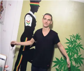 ??  ?? Jude poses in front of his ‘police and ganja plant’ painting at Jude Rude exhibition on December 14 at Spanish Court Hotel.