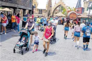  ??  ?? Masked visitors walk around Hogsmeade at The Wizarding World of Harry Potter in Adventure during its official reopening on Friday, June 5, 2020.