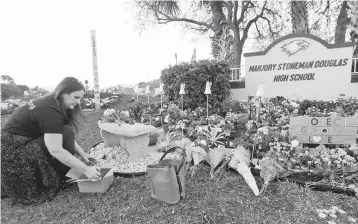  ?? WILFREDO LEE/AP ?? Suzanne Devine Clark, an elementary school art teacher, places painted stones in February 2019 at a memorial outside Marjory Stoneman Douglas High School on the first anniversar­y of the school shooting in Parkland, Florida.