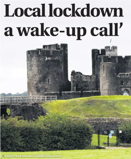 ??  ?? A man in a mask walks past Caerphilly Castle yesterday
