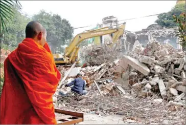  ?? HENG CHIVOAN ?? A Buddhist monk looks on as an excavator destroys old monastery buildings at Wat Ounalom in Phsar Kandal commune of the capital’s Daun Penh district on December 12.