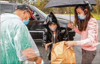  ??  ?? Pedro Barahona (left) takes Easter meals Thursday from Compassion Kitchen Project co-founders Isabel Rice (center) and Lisa Blanco at The Mission church in Atlanta.