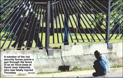  ?? ReuTeRs ?? A member of the riot security forces points a gun through the fence of an air force base at David Jose Vallenilla, who was fatally injured Thursday.