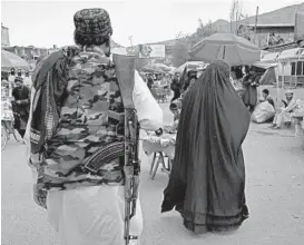  ?? EBRAHIM NOROOZI/AP ?? A woman wearing a burqa walks in the old market Sunday as a Taliban fighter stands guard in Kabul, Afghanista­n. Some Afghans questioned the latest Taliban edit.