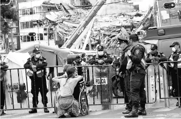  ??  ?? A woman who was rescued from a building on the same day it collapsed after the earthquake sits in a wheelchair and in front of a police blockade at the site of the same building, and where rescue teams continue to search for bodies trapped in the...