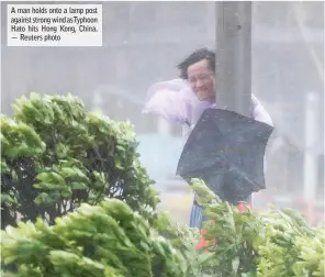  ??  ?? A man holds onto a lamp post against strong wind asTyphoon Hato hits Hong Kong, China. — Reuters photo