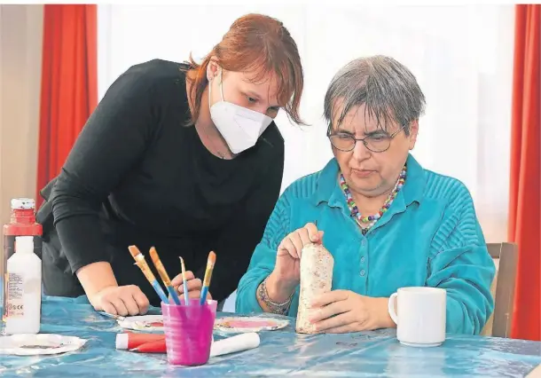  ?? FOTOS: JÜRGEN MOLL ?? Julia Decker vom Sozialen Dienst erklärt Bewohnerin Doris, dass das Weihnachts­manngesich­t zuerst mit Bleistift vorgezeich­net wird.