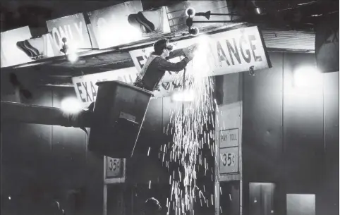  ?? Hearst Connecticu­t Media fille photo ?? A Connecticu­t Department of Transporta­tion employee in a bucket hoist uses a torch to cut bolts from a sign at the Stratford Toll Plaza on the turnpike minutes before tolls were eliminated on Oct. 9, 1985.