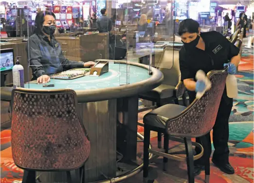  ?? GETTY IMAGES ?? Dealer Gina Khounphith­ack looks on as Eloina Marquez sanitizes the chairs at the Bellagio, which opened Thursday for the first time since March 17.