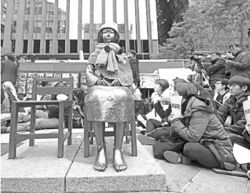  ?? — AFP photo ?? South Korean protesters sit near a statue of a teenage girl symbolisin­g former ‘comfort women’, who served as sex slaves for Japanese soldiers during World War II, during a weekly anti-Japanese demonstrat­ion in front of the Japanese embassy in Seoul.