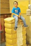  ??  ?? ■ Cruz Ferrusquia, grandson of Stephen and Judy Harris, sits atop the cotton bale at the Atlanta Museum. Such bales were reduced to about 500 pounds by huge compress machines for shipping by railroads to textile mills on the East Coast.