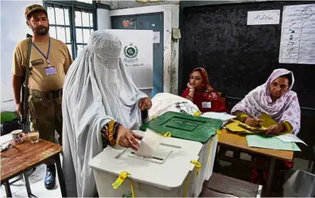  ?? — AFP ?? Making her vote count: A woman casting her ballot at a polling station amid tight security during the general election in Peshawar.