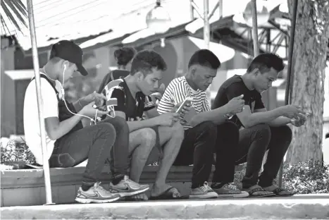  ?? MACKY LIM ?? HOOKED. With free Wi-Fi connection for the public, these men seem to be inseparabl­e from their mobile devices, browsing the internet while resting at Quezon Park in Davao City.