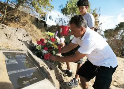  ??  ?? RAFAEL Rassi y su hijo Gustavo colocan un arreglo floral junto a la tarja que honrará la memoria de Alejandro Rafael Rassi, quien falleció hace 10 días tras ser arrastrado por las corrientes marinas.