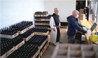  ??  ?? An employee wearing a protective facemask and gloves and Brother Godfried stand behind the plexiglass of the counter at the Westvleter­en beer shop of the Saint-Sixtus abbey.