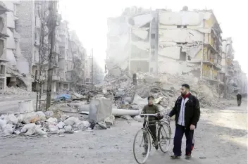  ?? — AFP ?? A Syrian man and a boy walk past destroyed buildings in Aleppo’s formerly rebel-held Al Shaar neighbourh­ood, a month after government forces retook the northern Syrian city from rebel fighters.