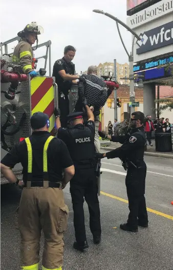  ?? DOUG SCHMIDT ?? Police officers take a suspect into custody after fire crews used an aerial ladder to bring him down from the roof of a building where two large air conditioni­ng units were tossed down into an alley below.