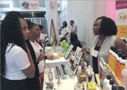  ?? T’CHA DUNLEVY ?? Volunteers Shanon Mathé and Séphora Bure get help from Sophia Murphy at her Roots to Curls booth at the Natural Hair Congress.