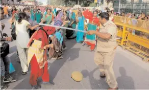  ??  ?? A policeman tries to disperse anganwadi workers protesting in front of Vidhan Bhavan in Lucknow on Tuesday.