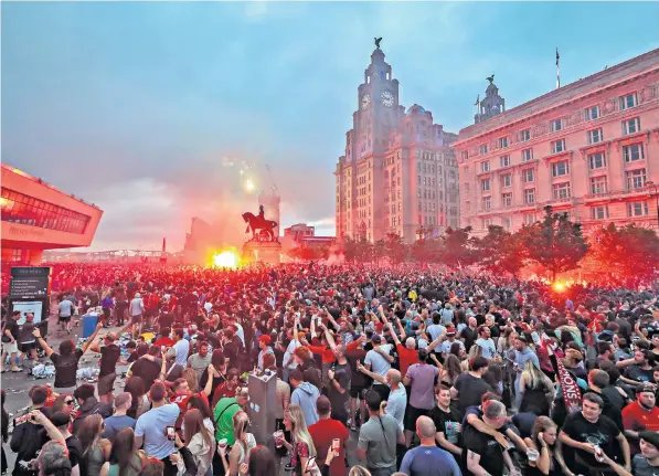  ??  ?? Liverpool fans let off flares outside the Liver Building in Liverpool on Friday following the team’s Premier League triumph, above, and workmen clear up rubbish left outside the building, left