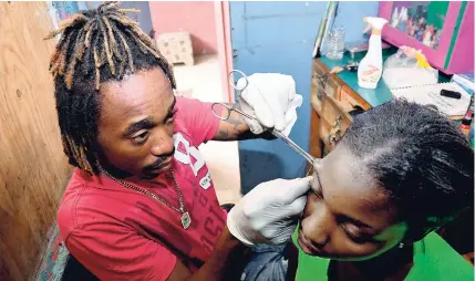  ??  ?? Orville ‘Spade’ Swaby focuses as he does a piercing on one of his clients.