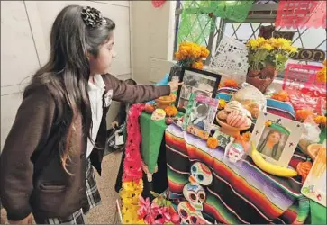  ?? Irfan Khan Los Angeles Times ?? LYLAH ROMERO, 8, places photos of loved ones on an altar this week at Calvary Cemetery. Over the years, she has honored family and pets. “I’ve lost a bunch of birds, a fish, a parrot, a dog and two turtles,” she says.