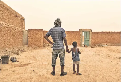  ??  ?? Thomas Howard, above, holds the hand of a friend’s child in Agadez, Niger. Above left, migrants expelled from Algeria play checkers in a transit camp while waiting to go home