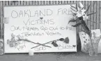  ??  ?? Signs and flowers in tribute to the fire victims adorn a fence near the site of a warehouse fire in Oakland.