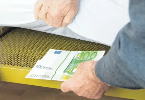  ?? FOTO: DPA ?? Ein Mann versteckt Bargeld unter einer Matratze: Nach einer neuen Studie des Bundesverb­andes deutscher Banken bewahren 20 Prozent der Sparer mehr als 500 Euro bar zu Hause auf. Elf Prozent davon haben einen Tresor. Die übrigen verstecken ihr Geld...