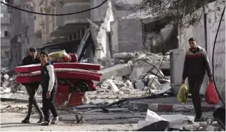  ?? ?? Palestinia­ns walk through destructio­n by the Israeli bombardmen­t in the Nusseirat refugee camp in Gaza Strip (January 2024)