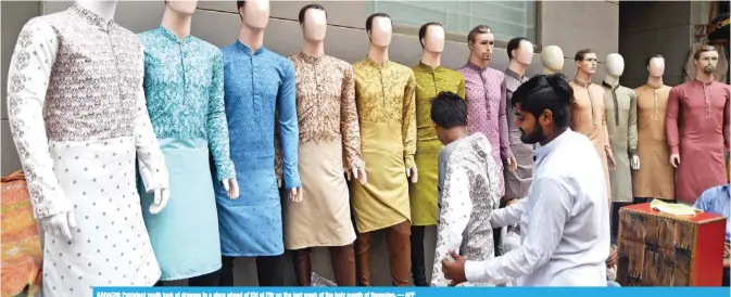  ?? — AFP ?? KARACHI: Pakistani youth look at dresses in a shop ahead of Eid ul Fitr on the last week of the holy month of Ramadan.