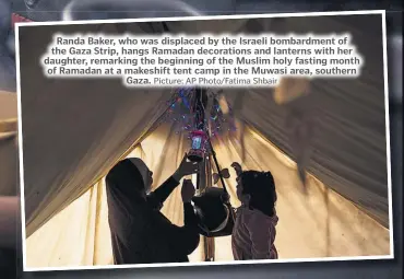  ?? Picture: AP Photo/Fatima Shbair ?? Randa Baker, who was displaced by the Israeli bombardmen­t of the Gaza Strip, hangs Ramadan decoration­s and lanterns with her daughter, remarking the beginning of the Muslim holy fasting month of Ramadan at a makeshift tent camp in the Muwasi area, southern Gaza.