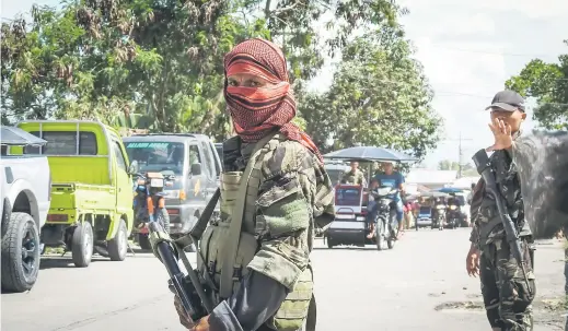  ?? — Gambar AFP ?? KINI SEKUTU: Seorang anggota MILF dengan muka bertutup ditemani seorang askar kerajaan (kanan) ketika memantau pos pemeriksaa­n mudah alih di Datu Salibo, Maguindana­o kelmarin.