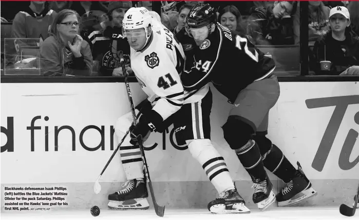  ?? JAY LAPRETE/AP ?? Blackhawks defenseman Isaak Phillips (left) battles the Blue Jackets’ Mathieu Olivier for the puck Saturday. Phillips assisted on the Hawks’ lone goal for his first NHL point.