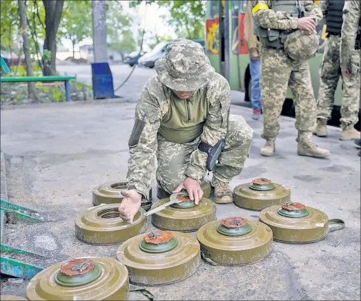  ?? ?? DANGEROUS JOB: A Ukrainian soldier (above) deactivate­s anti-tank mines before reposition­ing them to the frontline closer to Russian troops Sunday in Kharkiv. Below, a damaged tank sits on a shelled street in Mala Rohan village near Kharkiv.