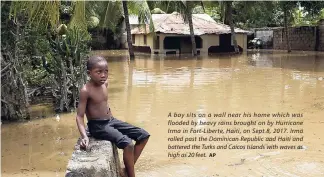 ?? AP ?? A boy sits on a wall near his home which was flooded by heavy rains brought on by Hurricane Irma in Fort-Liberte, Haiti, on Sept 8, 2017. Irma rolled past the Dominican Republic and Haiti and battered the Turks and Caicos Islands with waves as high as 20 feet.