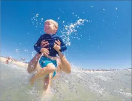  ??  ?? JAMES WILLIAMS of Northridge plays in the surf with his son, Kyle, 4, while vacationin­g at the family-owned Sea Sprite Motel in Hermosa Beach.