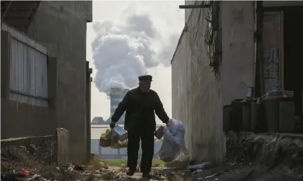  ?? (Thomas Peter/Reuters) ?? A MAN COLLECTS recyclable­s from an alley as smoke billows from the chimney of a factory in rural Gaoyi county, known for its ceramics production, near Shijiazhua­ng, China earlier this month.
