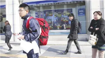  ?? — AP ?? TOKYO: People walk by an electronic stock board of a securities firm in Tokyo yesterday. Asian shares wavered yesterday, with the dollar’s recent weakness dampening sentiment among investors, who are also staying away from risky positions before the...