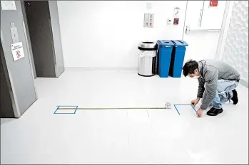  ?? STEVEN SENNE/AP ?? Kevin Gonzales places markings to promote social distancing May 21 near an elevator on the campus of Boston University.