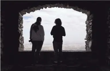  ??  ?? Noah Johnston, left, and Iovany de Leon look out at the city, haze obscured by high wind, on Monday from Dobbins Lookout at South Mountain in Phoenix.