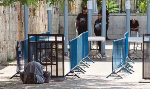  ??  ?? SEORANG penduduk Palestin menunaikan solat di hadapan pengesan logam di pintu masuk ke pekarangan Masjid Al-Aqsa. - EPA
