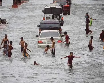  ??  ?? SEKUMPULAN kanak-kanak bermain di jalan raya yang
dinaiki air akibat ribut di Manila semalam. - AFP