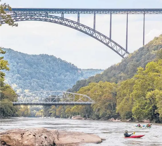  ?? TONY CENICOLA/THE NEW YORK TIMES PHOTOS 2018 ?? Kayakers paddle under the New River Gorge Bridge in Fayettevil­le, West Virginia. The gorge shows off millions of years of geological history.