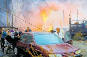  ?? AP ?? Residents push a car away from a burning forest fire engulfing homes in Villa Alemana, Valparaiso, Chile, on Friday.