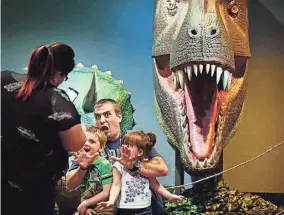  ?? THE COMMERCIAL APPEAL FILES ?? July 26, 2016: Derrick Bennett puts on his best scared-of-the-dinosaurs face while posing with his kids Serenity Bennett, right, and Lucian Bennett at the
Pink Palace’s “Scenes of Dinosaurs” exhibit during a free Tuesday at the museum.